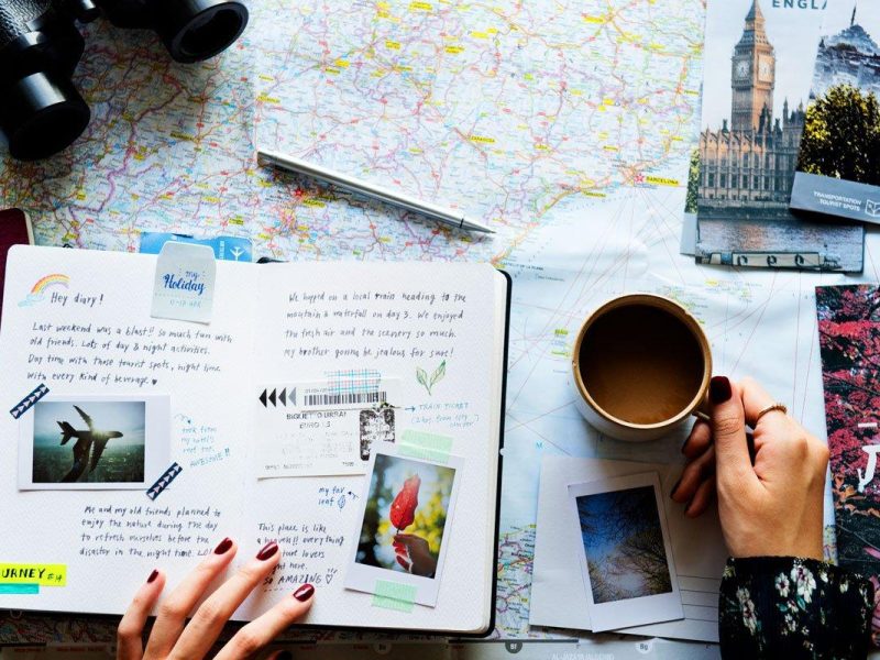 An open travel journal with postcards and a pen on a café table