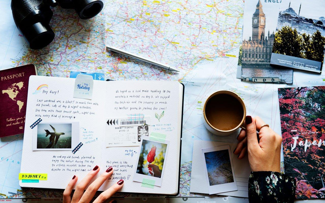 An open travel journal with postcards and a pen on a café table